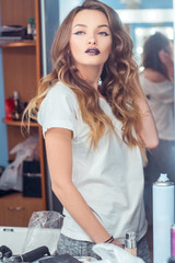 beautiful young girl with magenta lips and curly hairstyle posing across the mirror