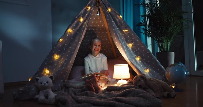 Girl reading book at night sitting in the wigwam
