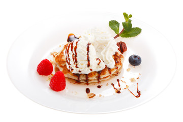 Serving pancakes with ice cream and whipped cream on the plate. Decorated with chocolate syrup, nuts and fresh berries and mint. Isolated on white background.