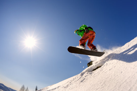 The snowboarder jumps from the springboard against the blue sky in the backlight.