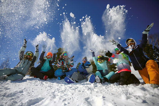 A group of friends of skiers and snowboarders fun throwing snow on top of the mountain.