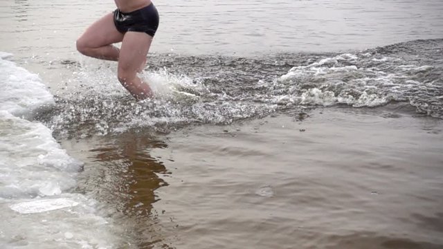 In slow motion, a person after bathing in icy water runs out onto the snow-covered shore