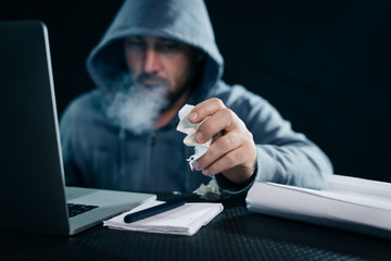 male hacker sitting in a room behind a laptop y smokes