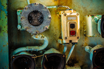 Broken and very old circular gauge and power switch with metal tube and electric wire inside the cockpit of abandoned navy ship.