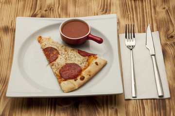 a piece of pizza Peperone on a plate served with ketchup