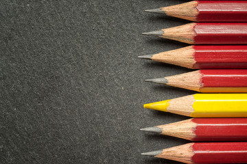 Yellow pencil standing out from crowd of plenty identical black fellows on black  table. Leadership, uniqueness, independence, initiative, strategy, dissent, think different, business success concept.