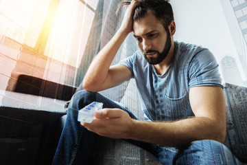 Strong headache. Sad man pressing lips and bowing head while looking at organizer for medicine