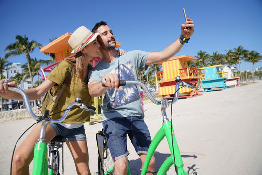 Young couple riding bikes in Miami beach, taking selfie pictures