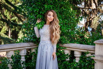 fashion outdoor photo of elegant beautiful woman with blond hair in luxurious sequins dress and silver accessories,posing in summer park