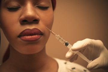 Close up portrait African middle age woman using injection for face lifting.