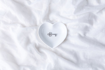 Ceramic dish in the shape of a heart with a key inside on the white background fabric