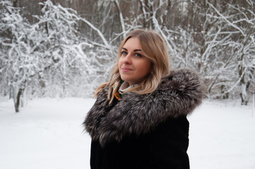 Smiling, joyful young woman in the winter in the park. Blonde in winter coat walking in park