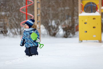 Мальчик с лопатой зимой на детской площадке
