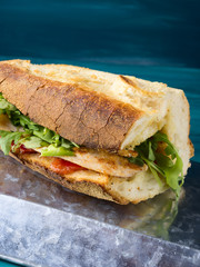 Hot sandwich with fresh Italian bread, grilled chicken breast, tomatoes and arugula on dark background