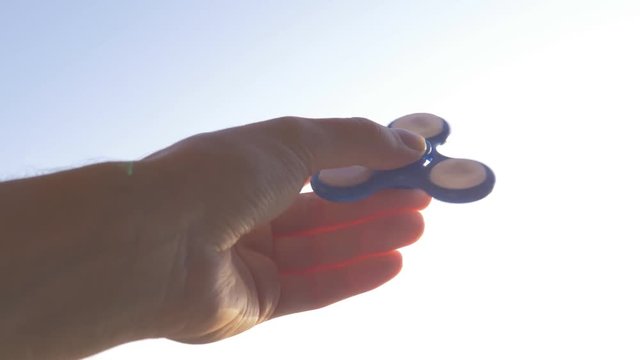 

Blue hand spinner or fidgeting spinner, rotating in hand. Bright sky background.