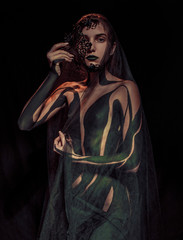 Beautiful young girl stands in transparent shawl with painted body and black mask in her hand. Body art.