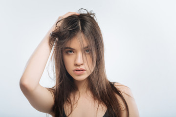 Family quarrel. Attractive smart carefree woman posing on the light 
 background while touching her  hair and staring  at the camera