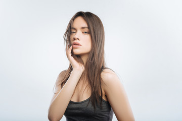 Fototapeta premium Stressful life. Elegant irresistible pleasant woman standing on the light background while planing arm on the chick and gazing at the camera