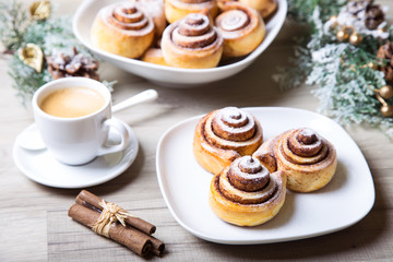 Fresh homemade buns with cinnamon, a cup of coffee, cinnamon sticks. Selective focus, close-up