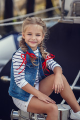 A beautiful little girl in a marine style against the backdrop of boats and yachts. Little Seaman