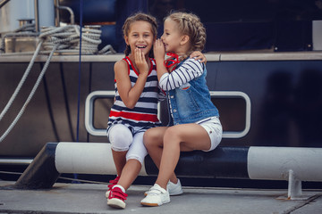 A beautiful little girl girlfriend in a marine style against the backdrop of boats and yachts. Idea and concept Friendship, vacations, rest