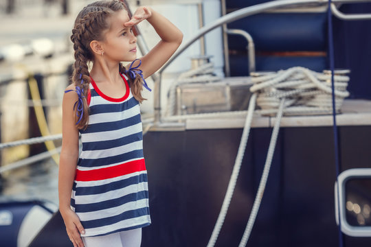 A beautiful little girl in a marine style against the backdrop of boats and yachts. Little Seaman