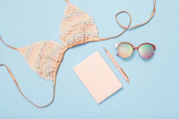 Beach holiday accessories, bikini, sunglasses, notebook on blue background, travel flat lay