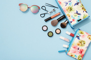 Beach holiday makeup flat lay on blue background,  eyeshadows, sunglasses, nail polish and makeup brushes