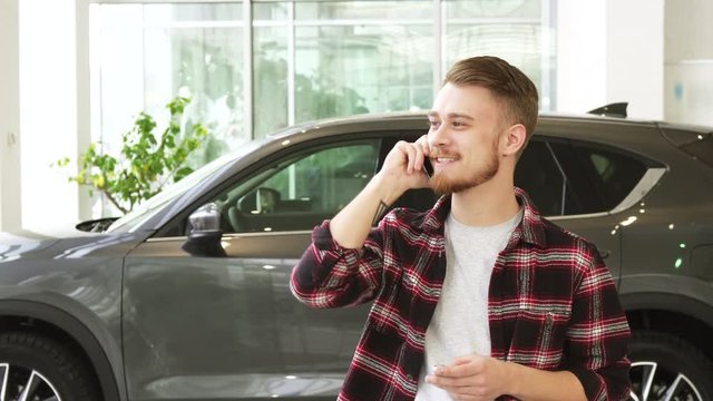 Happy young man talking on the phone after buying a new car at the dealrrship