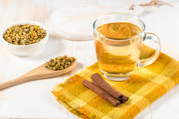 Cup of chamomile tea with dry chamomile flowers  on white wooden background.