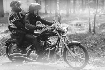 Obraz na płótnie Canvas Young romantic couple in a forest road on a motorcycle. Love, freedom, togetherness concept. Happy guy and girl travel on a motorbike, road trip adventure concept black and white