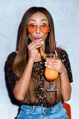 beautiful fashionable african american girl drinking cocktail and looking at camera