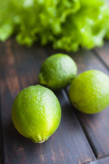 Diet, Healthy Food, Drink, Vegetarian Concept. Fresh whole green limes and lettuce leaves on a rustic wooden background