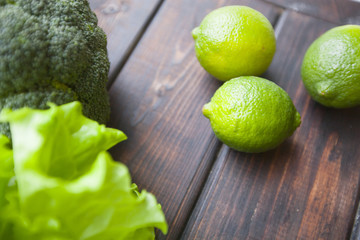 Diet, Healthy Food, Drink, Vegetarian Concept. Fresh whole green limes, broccoli and lettuce leaves on a rustic wooden background with copy space