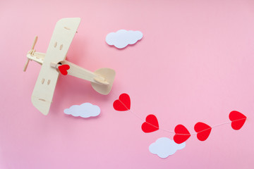 Happy Valentines day. wooden children's plane on a pink background with red heart, and garland in...