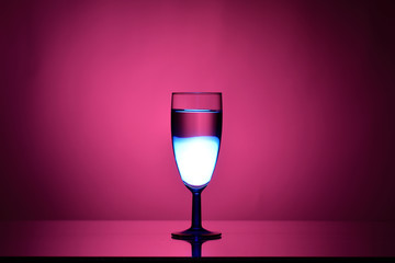 Wine in a glass goblet on a pink background with a gradient spot and stream of light on dark tones 