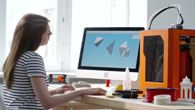 Tracking shot of talented female designer drafting 3D model on computer for printing it on 3D printer in small office