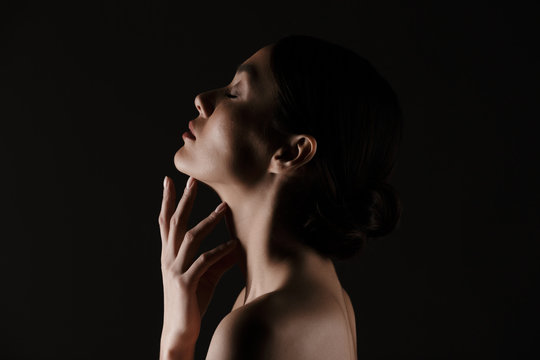 Beautiful image in profile of half-naked gentle woman posing on camera with closed eyes isolated, over black background