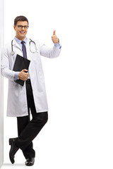 Doctor with a clipboard making a thumb up gesture and leaning against a wall