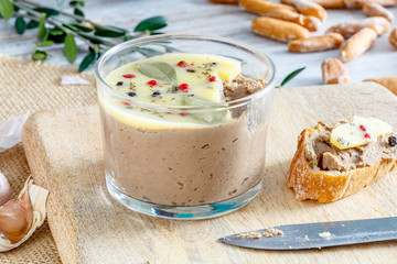 Chicken liver pate covered with melted butter and decorated with bay leaves and black and red pepper on rustic board. Front view.
