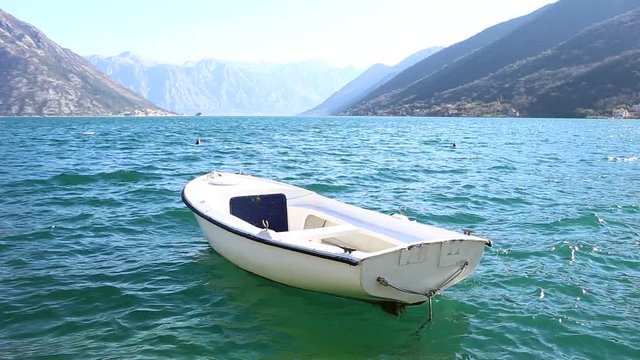 A white fishing boat rocks on the waves. Sunny day. Montenegro, Kotor Bay