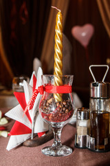 Romantic table decoration - golden candle in a glass with coffee seeds on the table