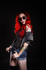 Close up of beautiful woman with tattoo wearing jeans short paint against black background.