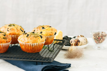 Savory muffins with olives and herbs on a wire rack on a white stone backdrop. Rustic style.