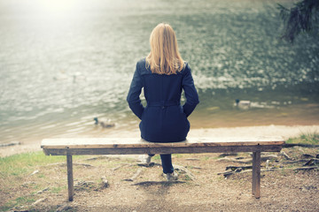 Model woman sitting on a wooden bench near the water. Rear view. - Powered by Adobe