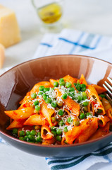 Tomato sauce and green peas penne pasta in a plate on a white stone background
