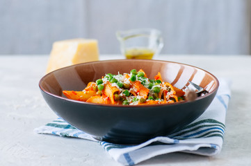 Tomato sauce and green peas penne pasta in a plate on a white stone background