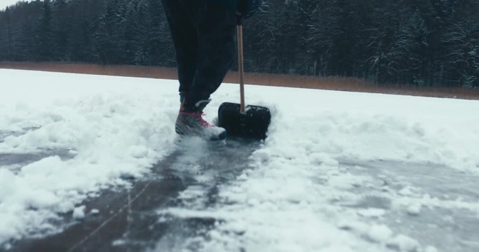 CU Male cleaning lake surface from snow before ice-skating and playing pond hockey. 4K UHD