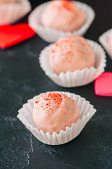 White chocolate and strawberry truffles on black stone background