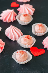 White chocolate and strawberry truffles and pink meringue kisses on black stone background